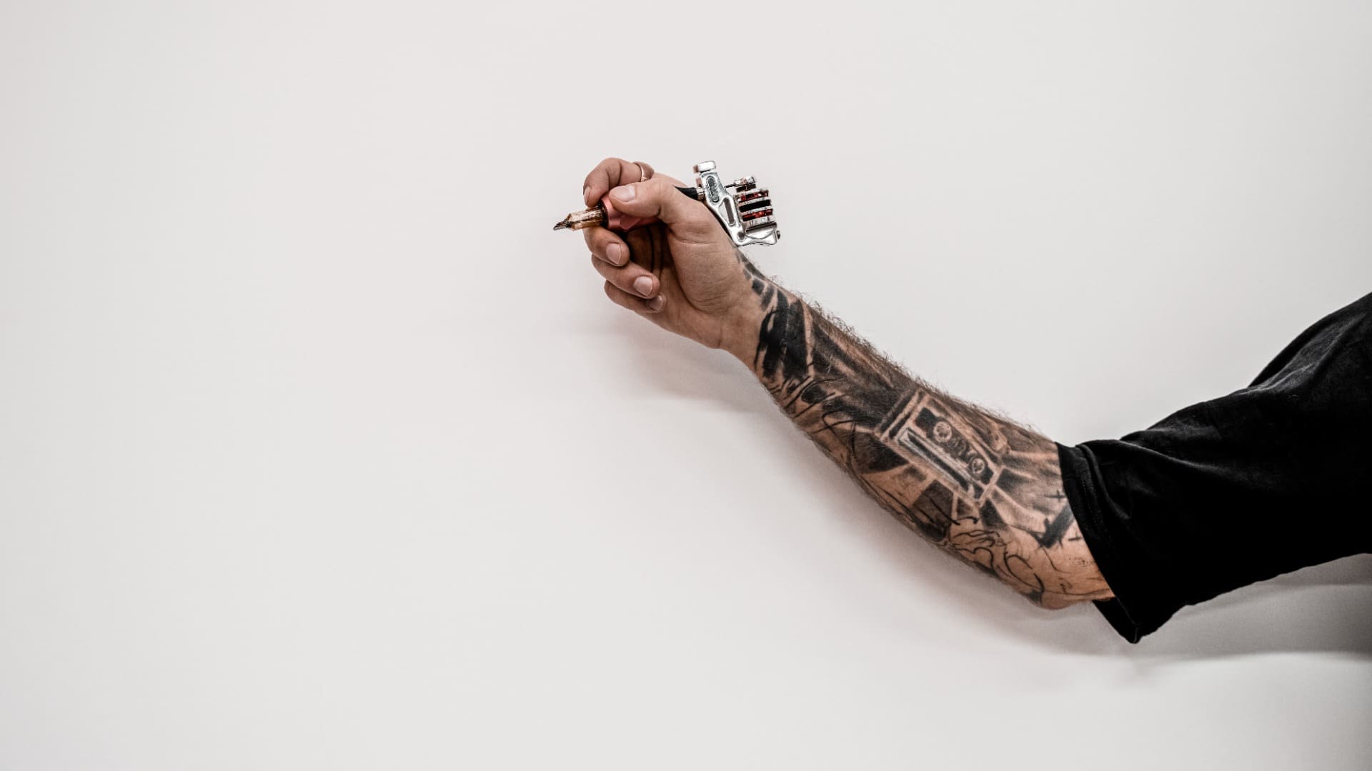 Primer plano de la mano del artista del tatuaje hipster anticuado que sostiene la máquina del tatuaje sobre un fondo blanco